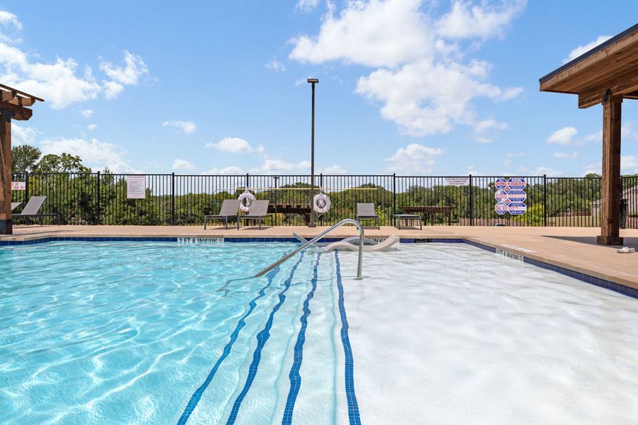 Outdoor community pool with lounge chairs, metal safety railing, and black iron fence surrounding the deck area.