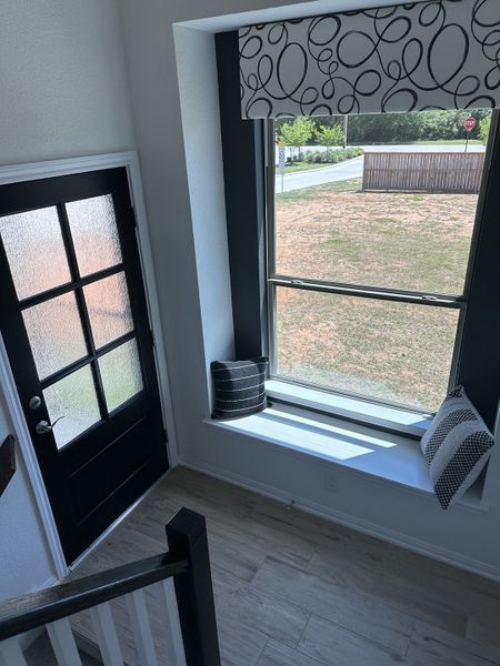 Bright entryway with a modern black door, large window seat, and stylish geometric valance, featuring light wood flooring. Bright entryway with a modern black door, large window seat, and stylish geometric valance, featuring light wood flooring.