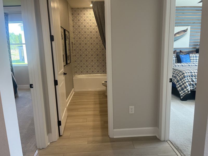 A hallway leads to a patterned-tile bathroom and a cozy bedroom with plaid bedding, offering a warm and inviting ambiance. A hallway leads to a patterned-tile bathroom and a cozy bedroom with plaid bedding, offering a warm and inviting ambiance.