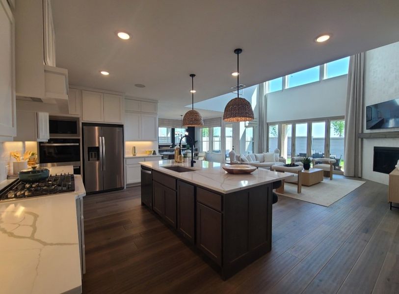 A spacious kitchen with dark wood flooring, large island, and ample natural light flowing into an elegant living area.