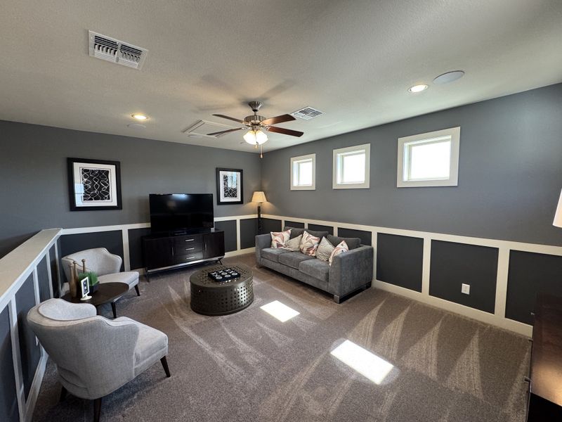 A cozy media room with a sleek gray sofa, matching armchairs, modern decor, and natural light through small windows.
