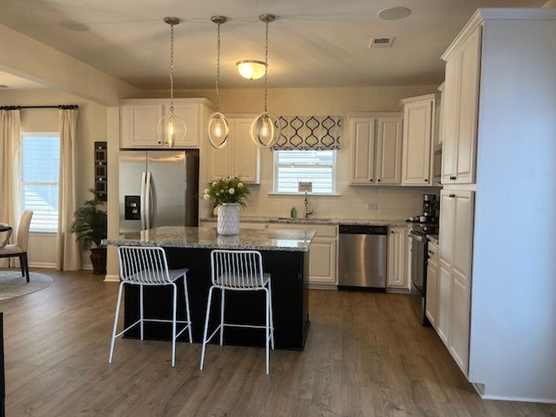 A modern kitchen with white cabinetry, stainless steel appliances, and a central island with pendant lighting.