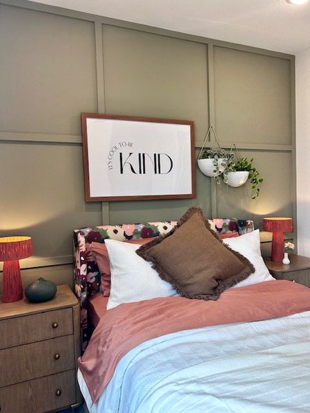 A cozy bedroom with a floral headboard, wood paneling, and vibrant decor, complemented by a "BE KIND" wall art.