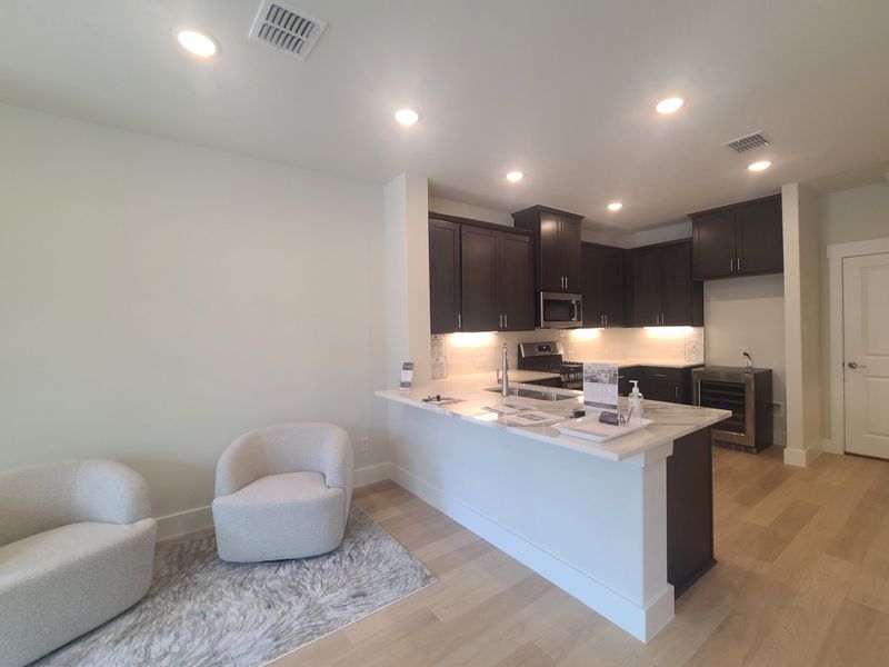 A modern kitchen with dark cabinetry, light countertops, recessed lighting, and cozy seating on a stylish rug.