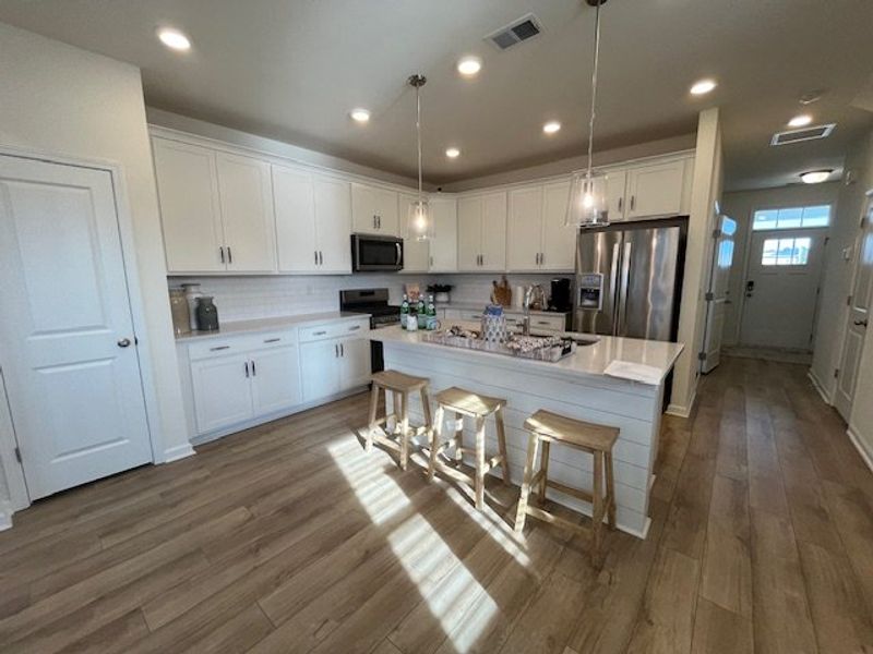 A modern kitchen featuring white cabinets, a spacious island with bar stools, and stainless steel appliances.