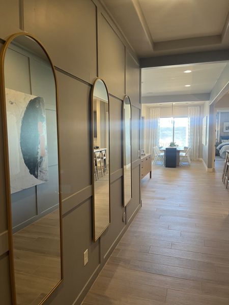 A modern hallway with elegant panel walls, arched mirrors, and natural light from a distant window.
