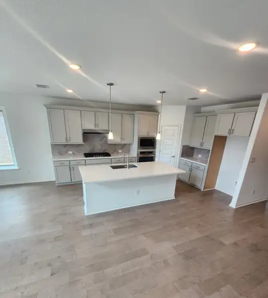 A modern kitchen with sleek cabinetry, a central island, pendant lighting, and wood flooring. A modern kitchen with sleek cabinetry, a central island, pendant lighting, and wood flooring.