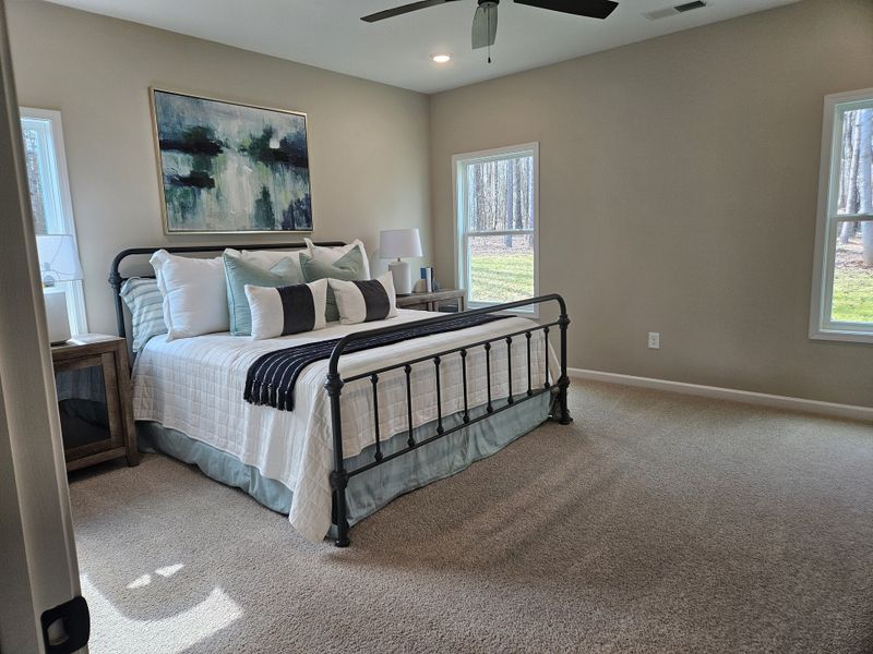 A modern bedroom with a black metal-framed bed, soft neutral decor, and large windows showing an outdoor view.