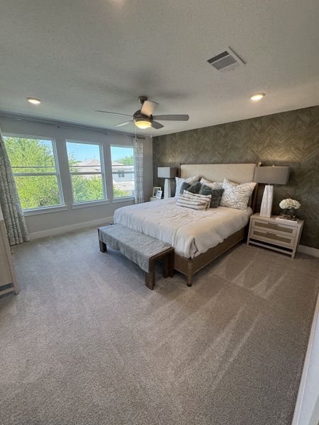 A serene bedroom featuring a cozy bed, textured accent wall, plush carpet, and large windows for ample natural light.