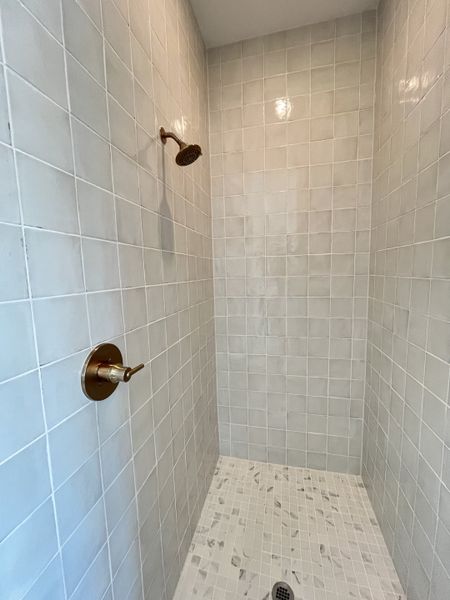 A sleek shower with elegant light tiles and modern bronze fixtures, offering a minimalist design. A sleek shower with elegant light tiles and modern bronze fixtures, offering a minimalist design.
