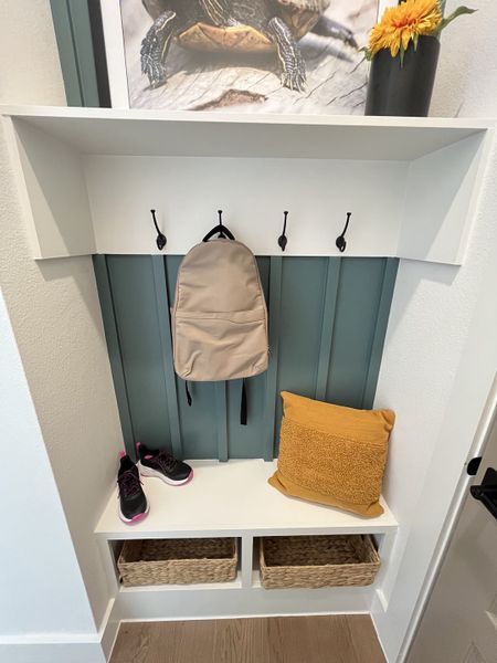 A functional entryway nook with a teal accent wall, hooks, and storage baskets, featuring a cozy pillow and bright decor. A functional entryway nook with a teal accent wall, hooks, and storage baskets, featuring a cozy pillow and bright decor.