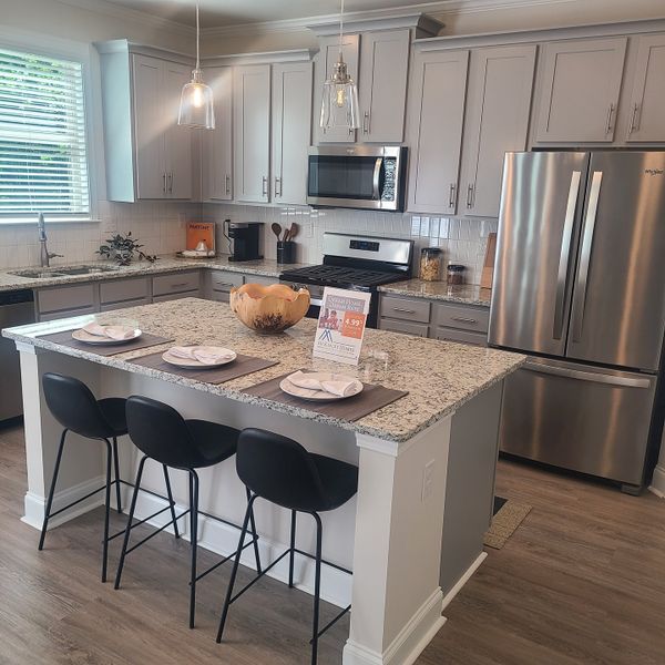 A modern kitchen featuring a granite island, stainless appliances, pendant lighting, and sleek cabinetry.