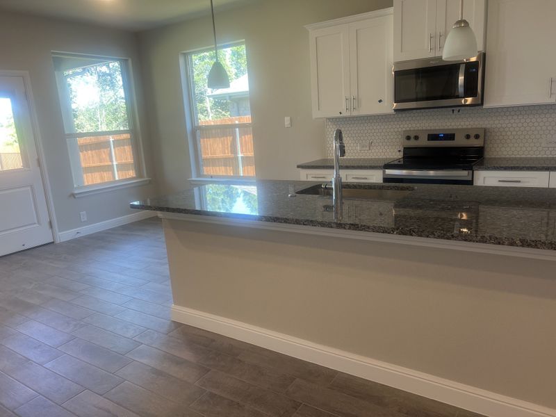 A modern kitchen with sleek granite countertops, white cabinetry, and stainless steel appliances, illuminated by pendant lights. A modern kitchen with sleek granite countertops, white cabinetry, and stainless steel appliances, illuminated by pendant lights.