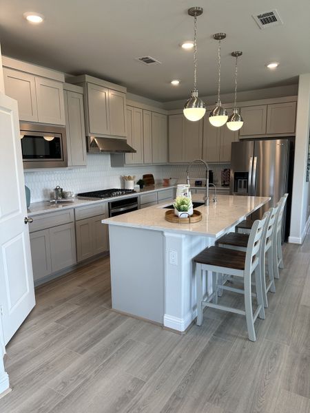 A modern kitchen with sleek gray cabinets, a large island, pendant lighting, and stainless steel appliances. A modern kitchen with sleek gray cabinets, a large island, pendant lighting, and stainless steel appliances.