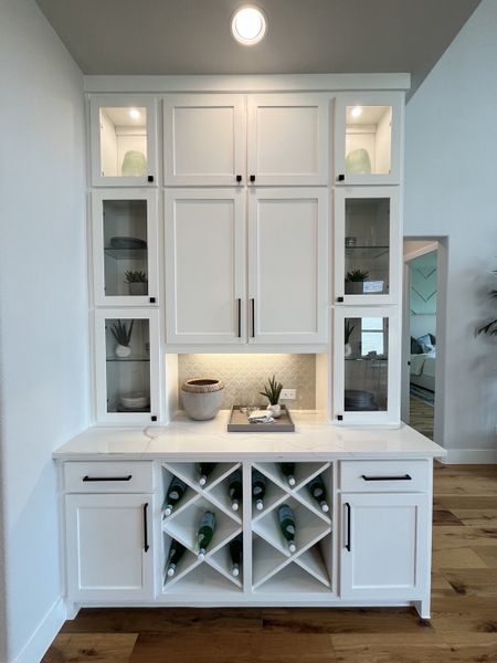 A chic wine bar with white cabinetry, glass doors, and ambient lighting, perfect for entertaining in style.