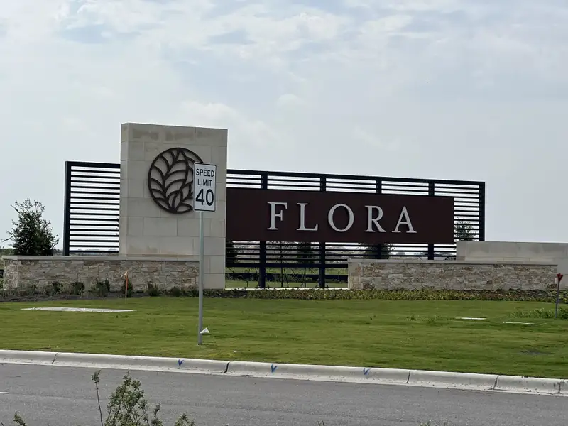 Entrance to Flora - 60' by Westin Homes in Hutto, TX, featuring a sleek sign and manicured landscaping.