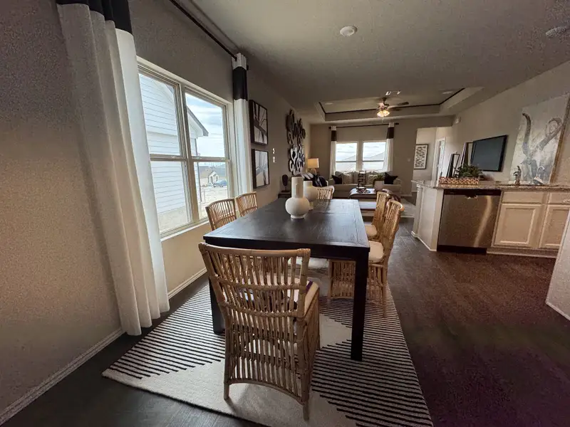 A cozy dining area with a dark wood table, wicker chairs, large window, and open view into the living room.