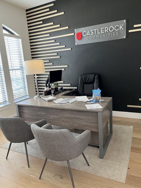 A modern office with a sleek desk, gray chairs, and an accent wall with the CastleRock Communities logo.