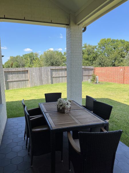 A charming patio with a wooden table, wicker chairs, and lush green views in a fenced backyard. Ideal for outdoor dining.