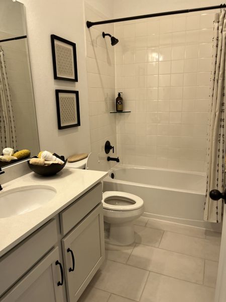 A cozy bathroom with a sleek white vanity, a tiled bathtub, elegant fixtures, and tasteful framed art pieces. A cozy bathroom with a sleek white vanity, a tiled bathtub, elegant fixtures, and tasteful framed art pieces.