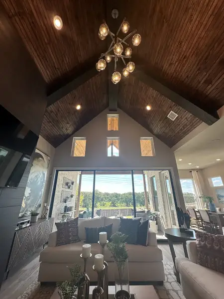 A luxurious living room with vaulted wooden ceilings, a chic chandelier, and expansive glass doors to the patio. A luxurious living room with vaulted wooden ceilings, a chic chandelier, and expansive glass doors to the patio.