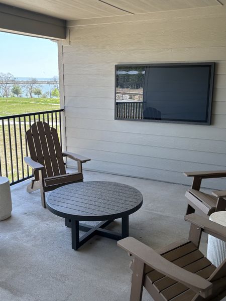 A cozy patio with Adirondack chairs, round table, and wall-mounted TV, offering a scenic view of the landscape beyond.