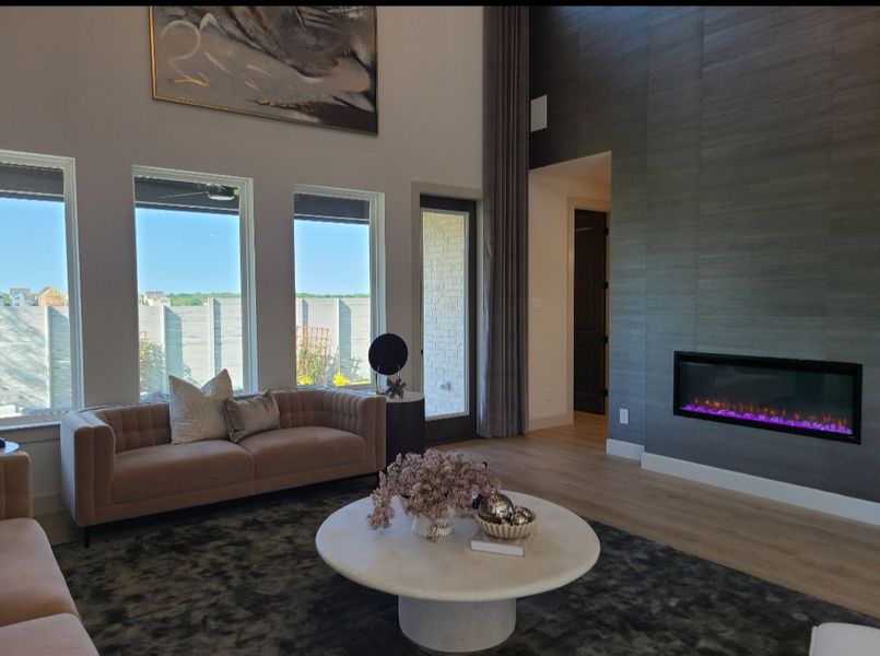 A modern living room featuring a sleek electric fireplace, chic sofas, and large windows brightening the space.