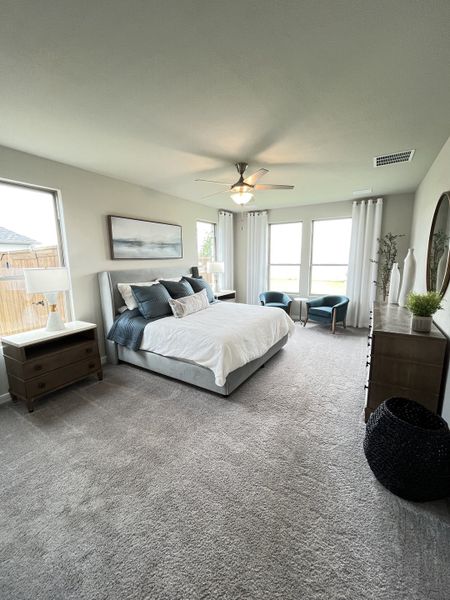 A cozy bedroom with plush carpeting, a comfy bed, elegant decor, and ample natural light from large windows.