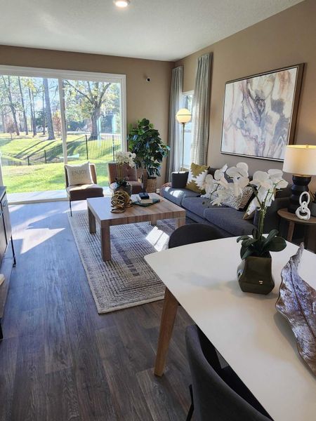 A cozy living room with large windows, wood floors, and modern decor, offering a serene view of the outdoors.