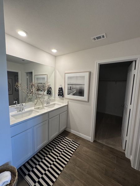 A modern bathroom with dual sinks, elegant decor, wooden flooring, and bright lighting for a refreshing ambiance.