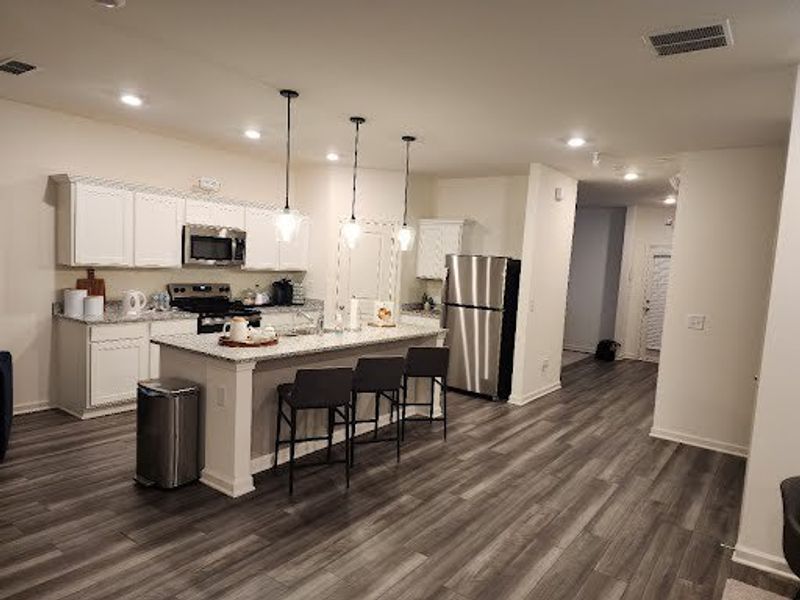 A modern kitchen with white cabinets, stainless steel appliances, pendant lighting, and sleek gray flooring.