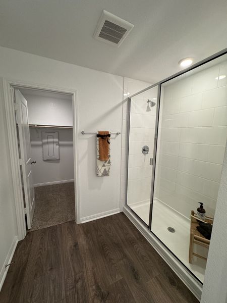 A modern bathroom with a sleek glass shower, dark wood flooring, and a walk-in closet for added convenience.