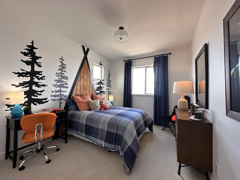 A cozy bedroom with tree-themed wall art, plaid bedding, and a playful orange desk chair. Modern and inviting decor.