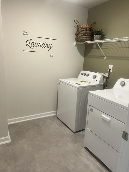 Modern laundry room with a washer, dryer, decorative basket, and tiled flooring.
