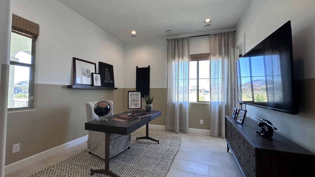 A modern home office with a sleek desk, wall-mounted TV, elegant decor, and natural light streaming through sheer curtains.