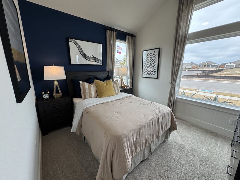 A cozy bedroom with a bold navy accent wall, plush bedding, modern furniture, and large windows offering natural light.
