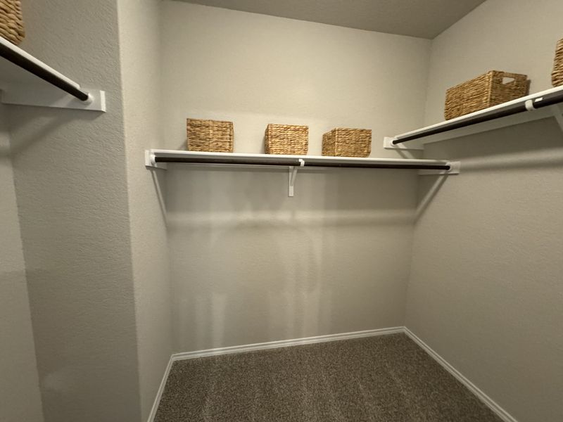 A spacious walk-in closet with carpeted flooring, shelves, and wicker storage baskets for organized living.