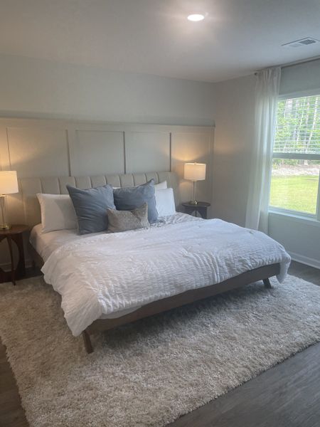 A cozy bedroom featuring a plush rug, elegant king-size bed, bedside tables with lamps, and natural light streaming through the window.
