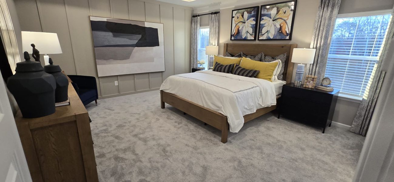 A cozy bedroom with soft carpeting, stylish artwork, and a neutral palette accented by vibrant yellow pillows.
