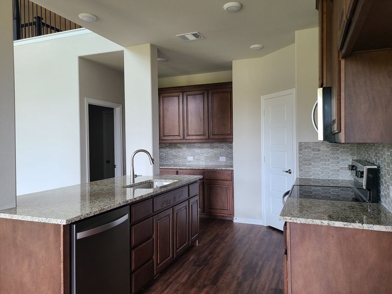 A modern kitchen with granite countertops, wood cabinets, and sleek stainless steel appliances.