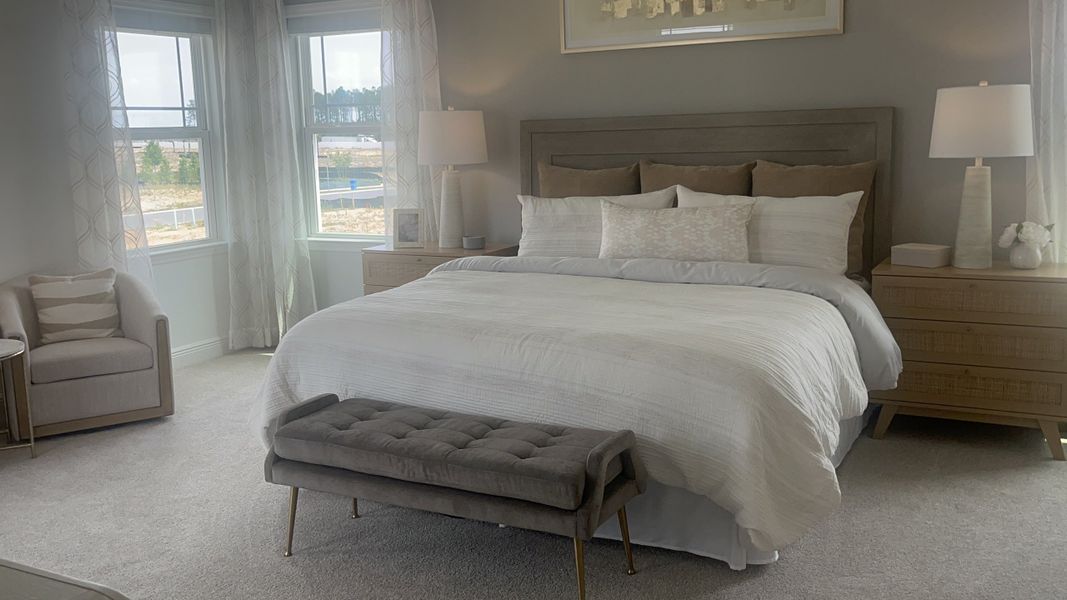A cozy bedroom featuring a plush bed, stylish bench, and elegant lamps, with ample natural light from large windows.