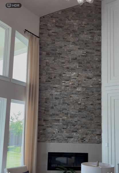 A grand living room with a floor-to-ceiling stone accent wall and large windows, providing an airy and elegant atmosphere. A grand living room with a floor-to-ceiling stone accent wall and large windows, providing an airy and elegant atmosphere.