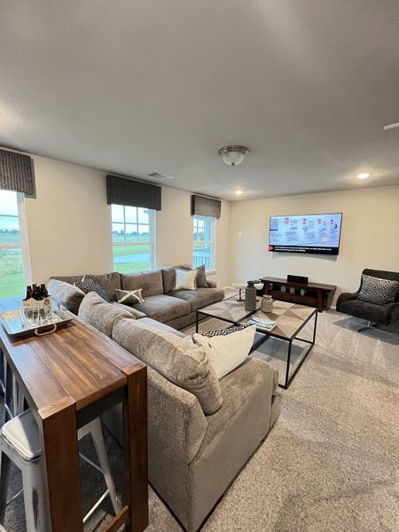 A cozy living room featuring a spacious sectional, large TV, and abundant natural light from multiple windows.