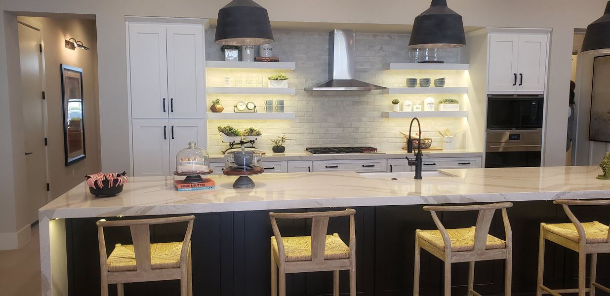 A modern kitchen with sleek white cabinets, open shelving, and a large island featuring pendant lighting and stylish seating.