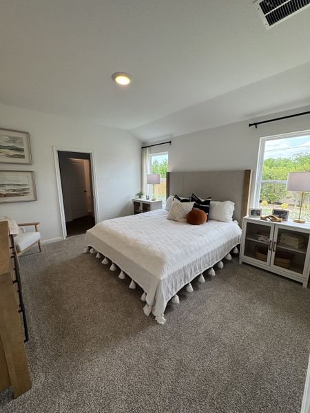 A cozy bedroom featuring a plush carpet, modern decor, and ample natural light from large windows.