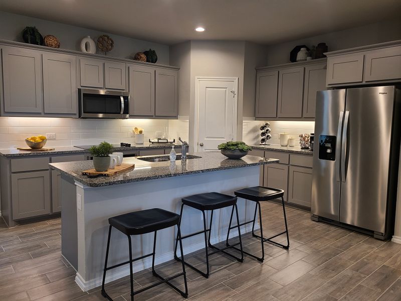 A modern kitchen with gray cabinets, sleek appliances, and a central island featuring bar seating and stylish decor.