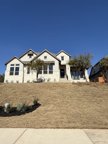 An elegant home with a grand entry, light stone exterior, and large windows in Lakeside at Tessera by Coventry Homes (Lago Vista, TX).