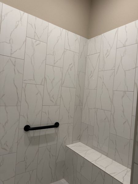 A sleek shower with marble-effect tiles and a convenient black grab bar for modern elegance. A sleek shower with marble-effect tiles and a convenient black grab bar for modern elegance.