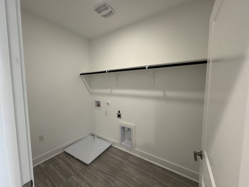 A spacious laundry room with a washing machine hookup, utility shelf, and sleek gray tile flooring. A spacious laundry room with a washing machine hookup, utility shelf, and sleek gray tile flooring.