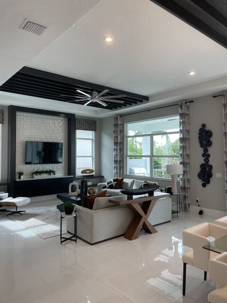A modern living room featuring a sleek ceiling fan, plush seating, and natural light through large windows.
